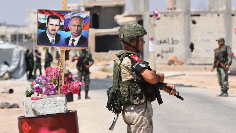 Putinova i Asadova slika na transparentu iza naoružanog vojnika
