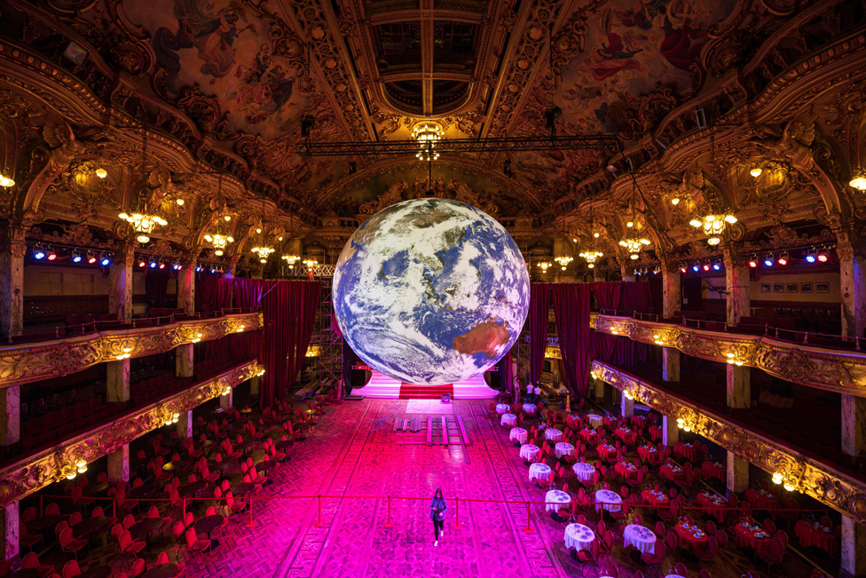 Members of the public admire an illuminated art installation looking like the earth