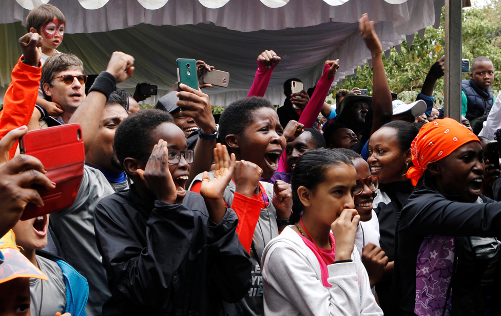 People celebrate as they watch Eliud Kipchoge run a marathon