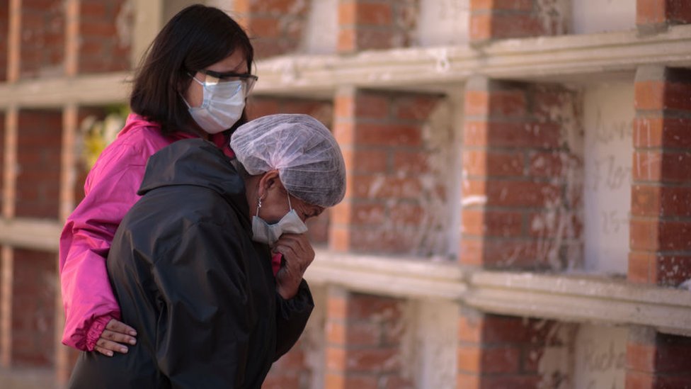 Two women wearing face masks mourn at a cemetery in La Paz, Bolivia