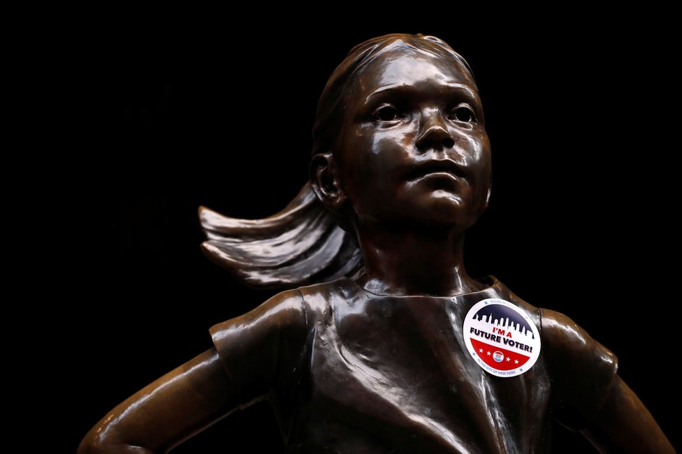 A statue of a girl with a voting sticker on it