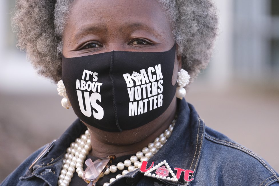 A woman wears a Black Voters Matter mask and looks to the camera