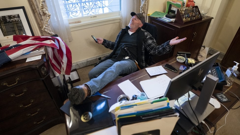 A supporter of US President Donald Trump sits at the desk of US House Speaker Nancy Pelosi