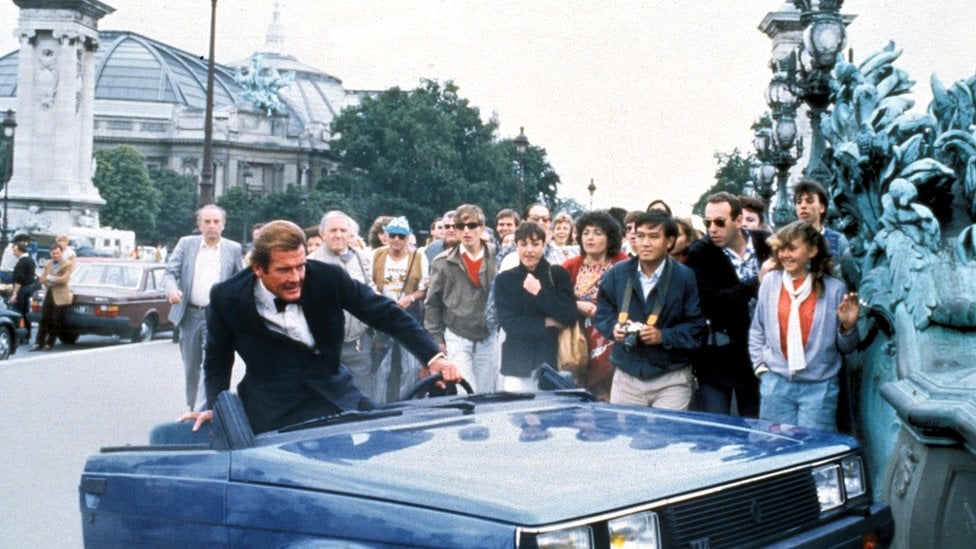 In this scene from the film of A View to a Kill, Roger Moore as Bond clambers out of a wrecked Renault car