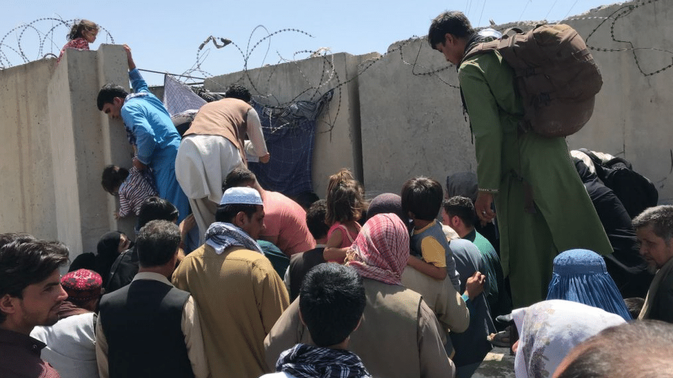 People struggle to cross the boundary wall of Hamid Karzai International Airport