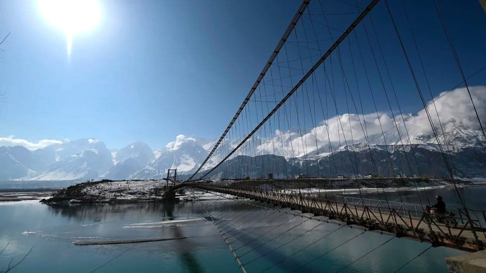 A bridge over the Indus river with views of glaciers in the background