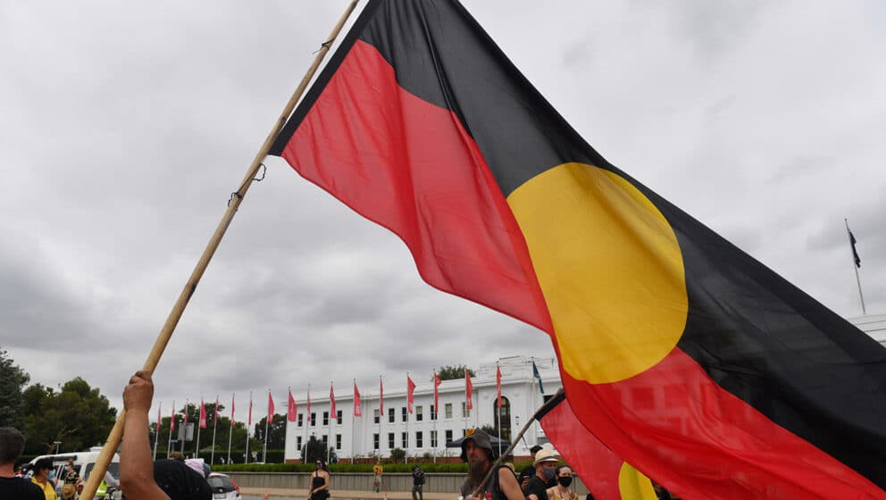 n indigenous protesters holds a flag in front of Old Parliament House, marking the 50th anniversary of The Aboriginal Embassy, in Canberra, Australia