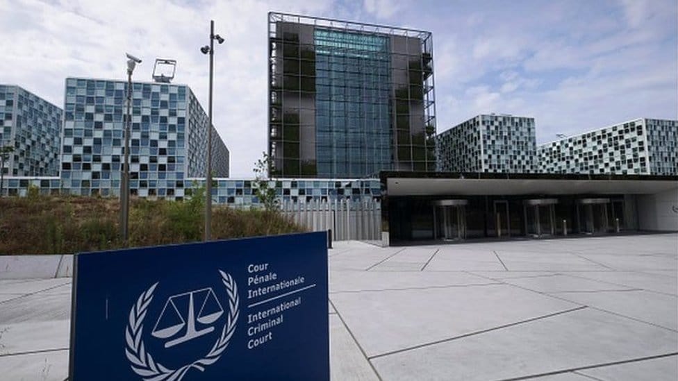 A set of glass modern buildings with a sign in front reading 'International Criminal Court'