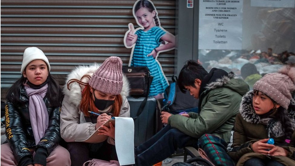 Refugees sit and wait to be collected