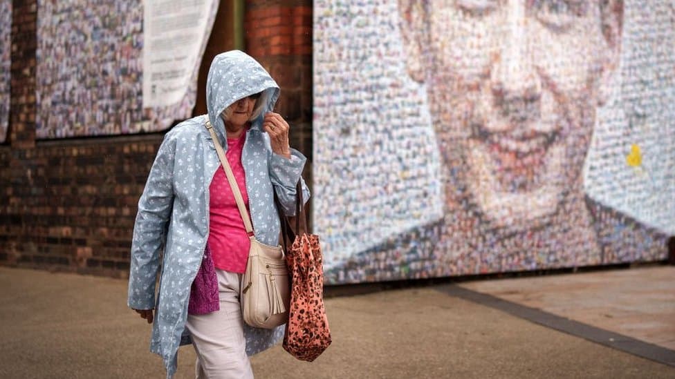 Woman walking in rain in front of street art.