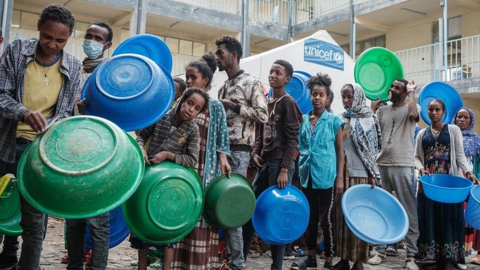 People who fled the violence in Ethiopia's Tigray region wait to receive injeras, Ethiopia's staple food of sour fermented flatbread, from their kitchen as only meal of the day at May Weyni secondary school, now hosting 10500 displaced people as an IDP camp, in Mekele, the capital of Tigray region, on June 19, 2021