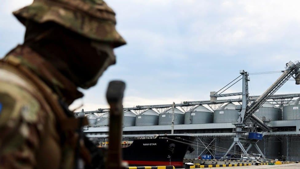 A Ukrainian serviceman stands in front of silos of grain from Odesa Black Sea port, 29 July 2022