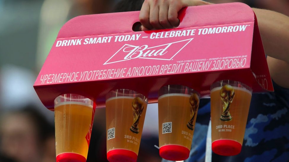 A fan hold a container with four glasses of Budweiser in it