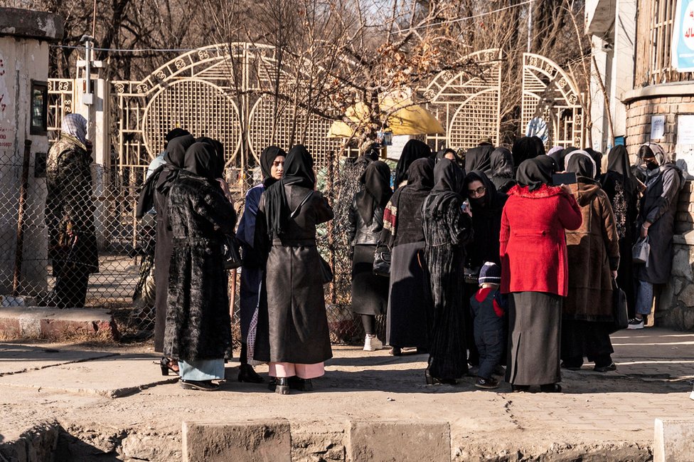 Afghan female university students stop by Taliban security personnel stand next to a university in Kabul on December 21, 2022.