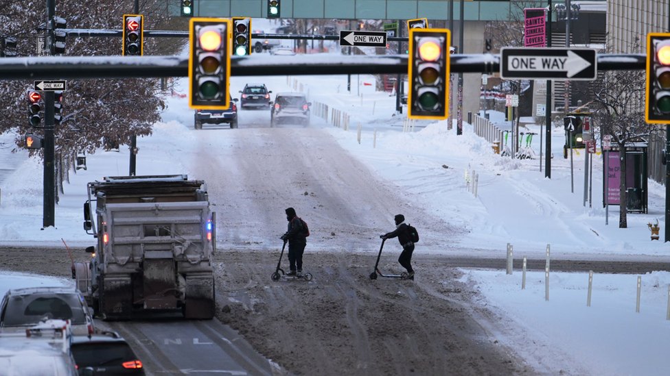 Snow on streets as people cross intersection.