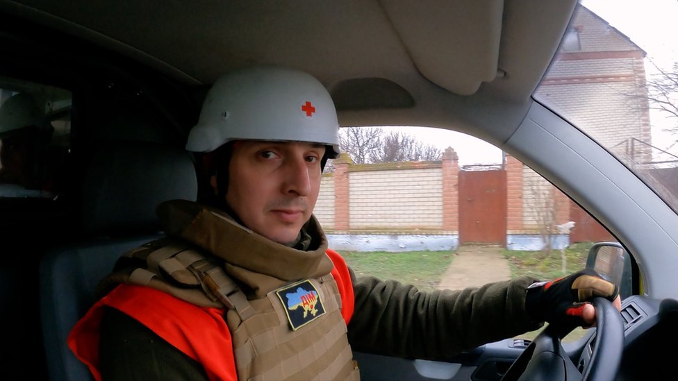 Red Cross volunteer Dmitro sits in his car, wearing protective gear