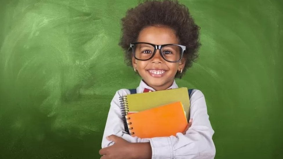 A smiling child with glasses and notebooks