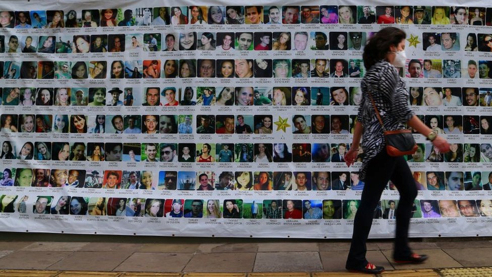 A woman walks past a banner with pictures of the people who died in the Kiss nightclub fire