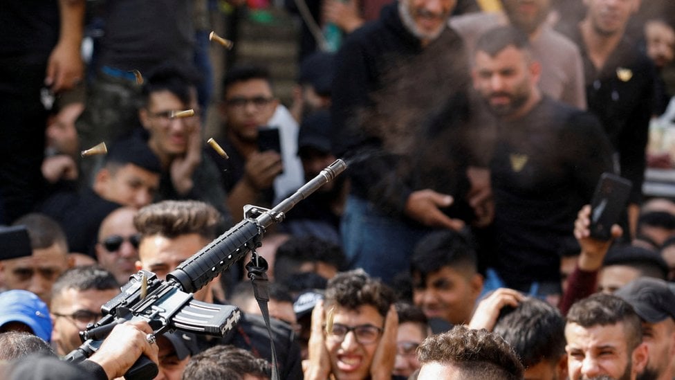 A gunman fires a weapon in the air as mourners attend the funeral of member of Palestinian group Lions' Den