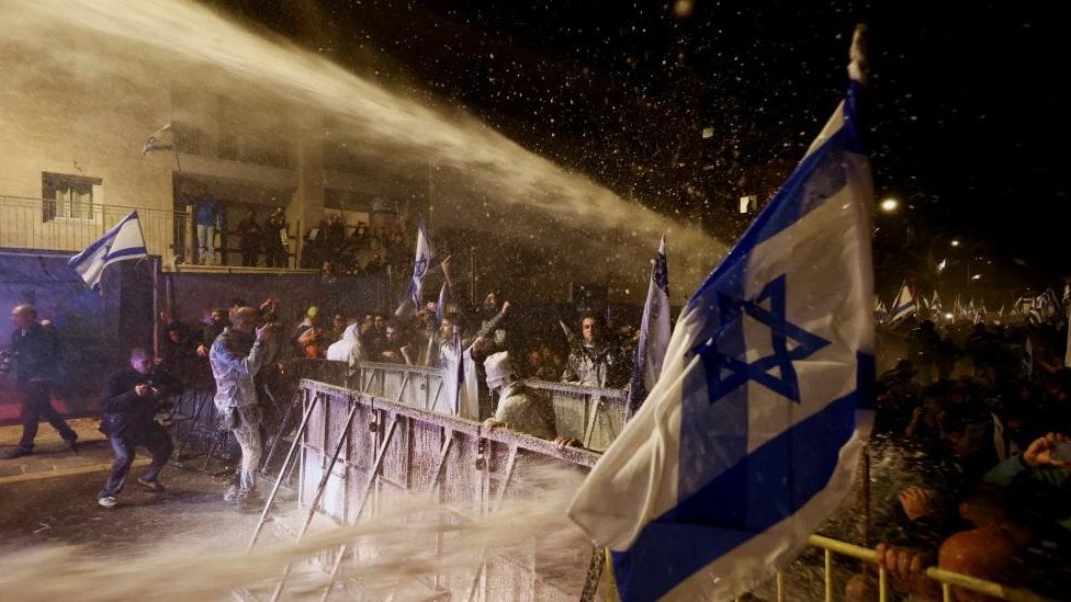 Protesters duck below a stream of water fired from a water canon