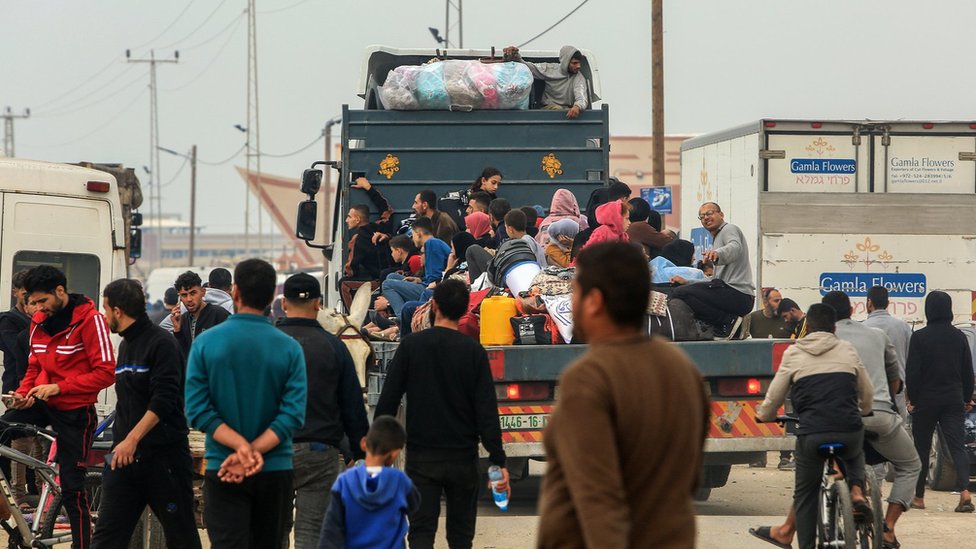 Displaced Palestinians ride on the back of a vehicle