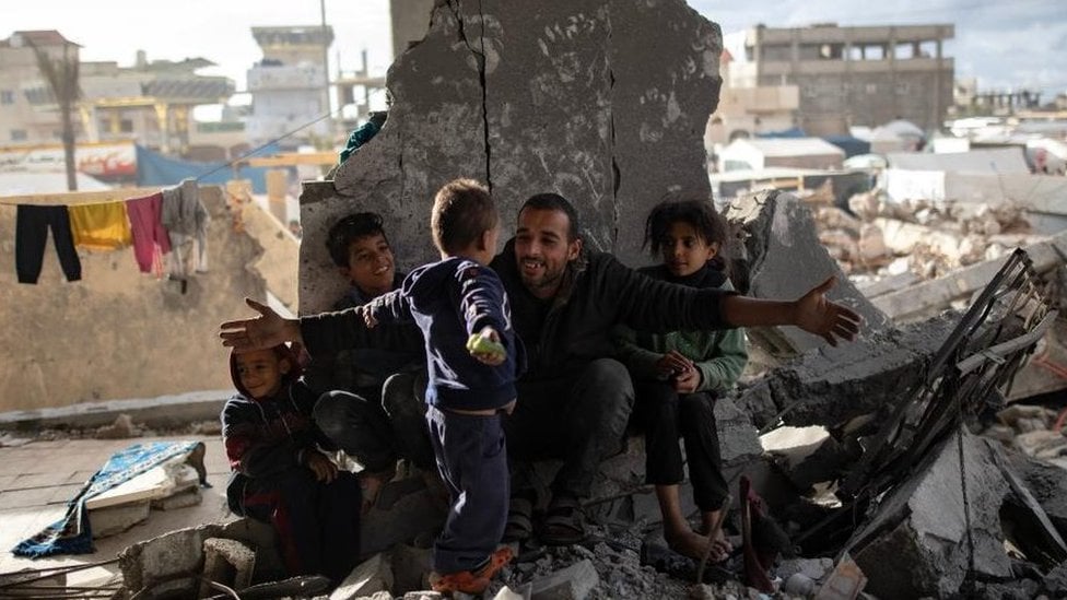 Displaced Palestinian Muhammad Al-Durra, 41, hangs clothes as he speaks to one of his children at the destroyed house they took shelter in, in the city of Rafah, south of the Gaza Strip, 11 January 2024