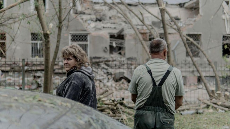 Žena i muškarac stoje ispred ruševina u Harkovu