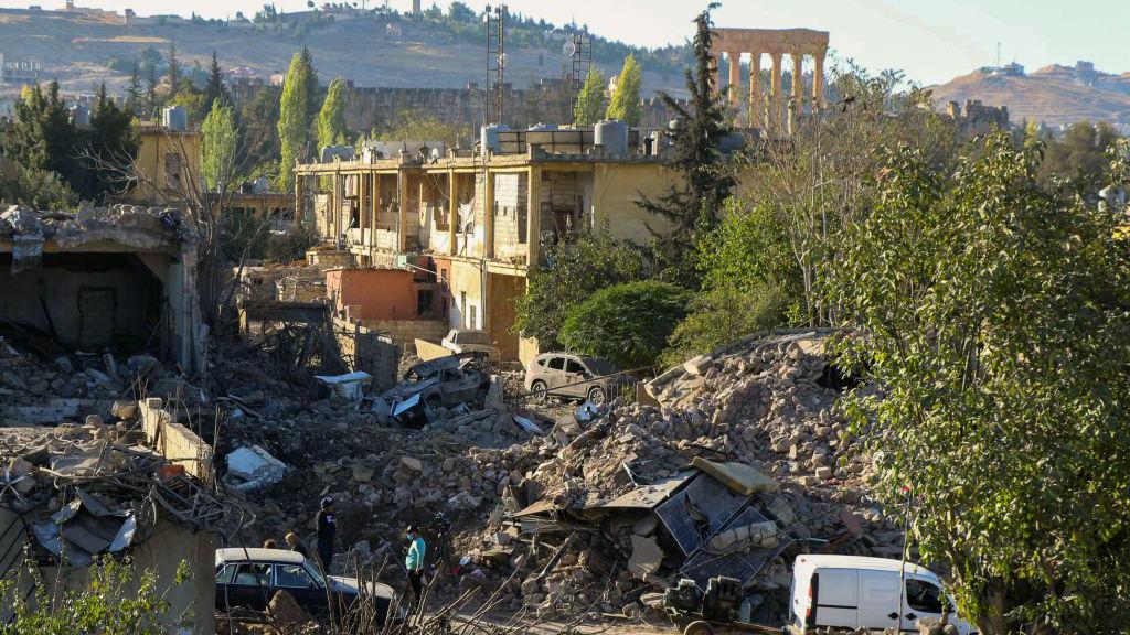 People inspect the destruction at the site of an Israeli air strike on the Gouraud Barracks area of Baalbek, with the city's Roman ruins visible in the background (29 October 2024)