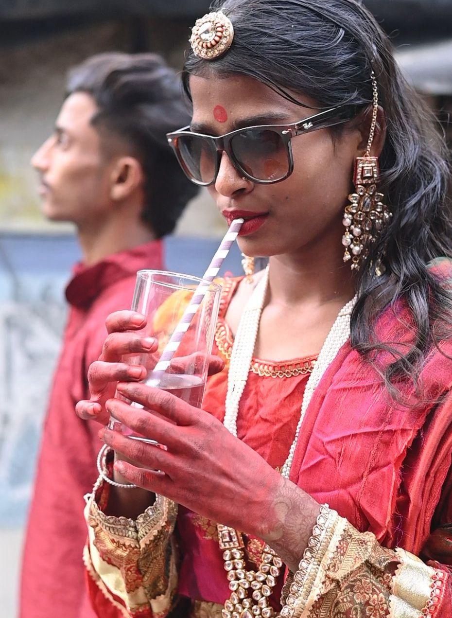 A girl drinks from a glass with a straw at a fashion show that has gone viral wearing colourful red clothing, jewellery and sunglasses