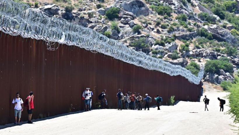 Migranti hodaju u SAD pored graničnog zida između SAD i Meksika u Jacumba Hot Springs, Kalifornija, jun 2024.