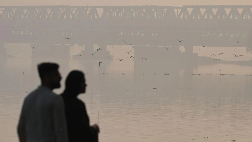 Silueta dvoje ljudi pored reke u zagađenom Delhiju