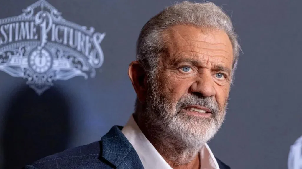 Glumac Mel Gibson sa sedom bradom, plavih očiju u odelu, gleda u kameru