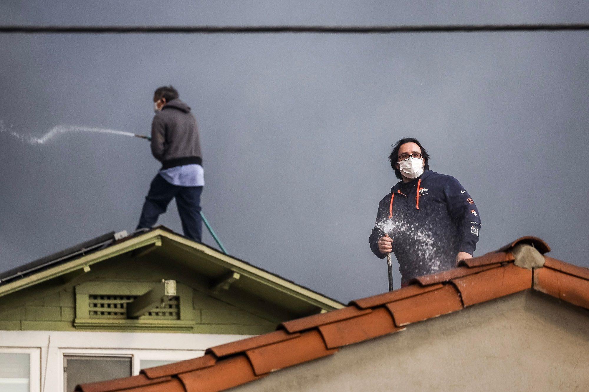 Muškarci s maskama gase malim šmrkovima požar sa krovova kuća